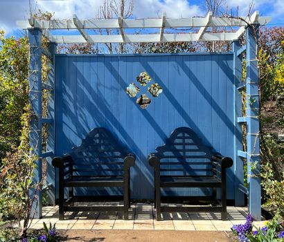 Compacte houten pergola in een kleine achtertuin met bistroset, klimplanten en lichte styling
